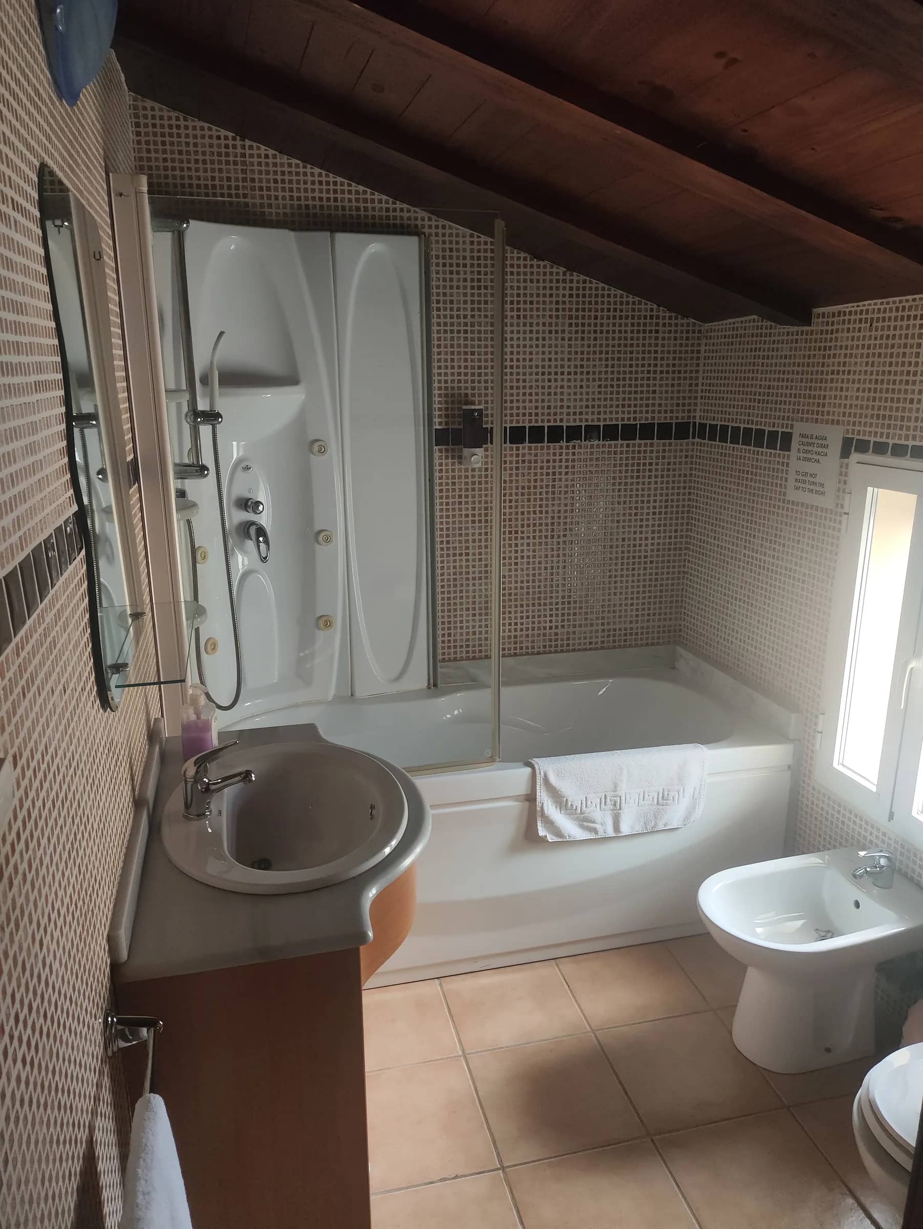 Baño con bañera, columna de hidromasaje y bidé bajo el techo de vigas