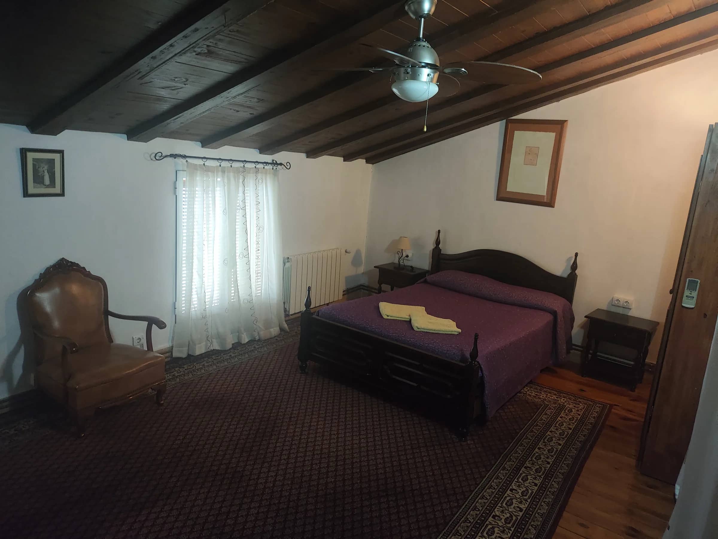 Habitación de matrimonio abuhardillada con vigas de madera, alfombra y butaca