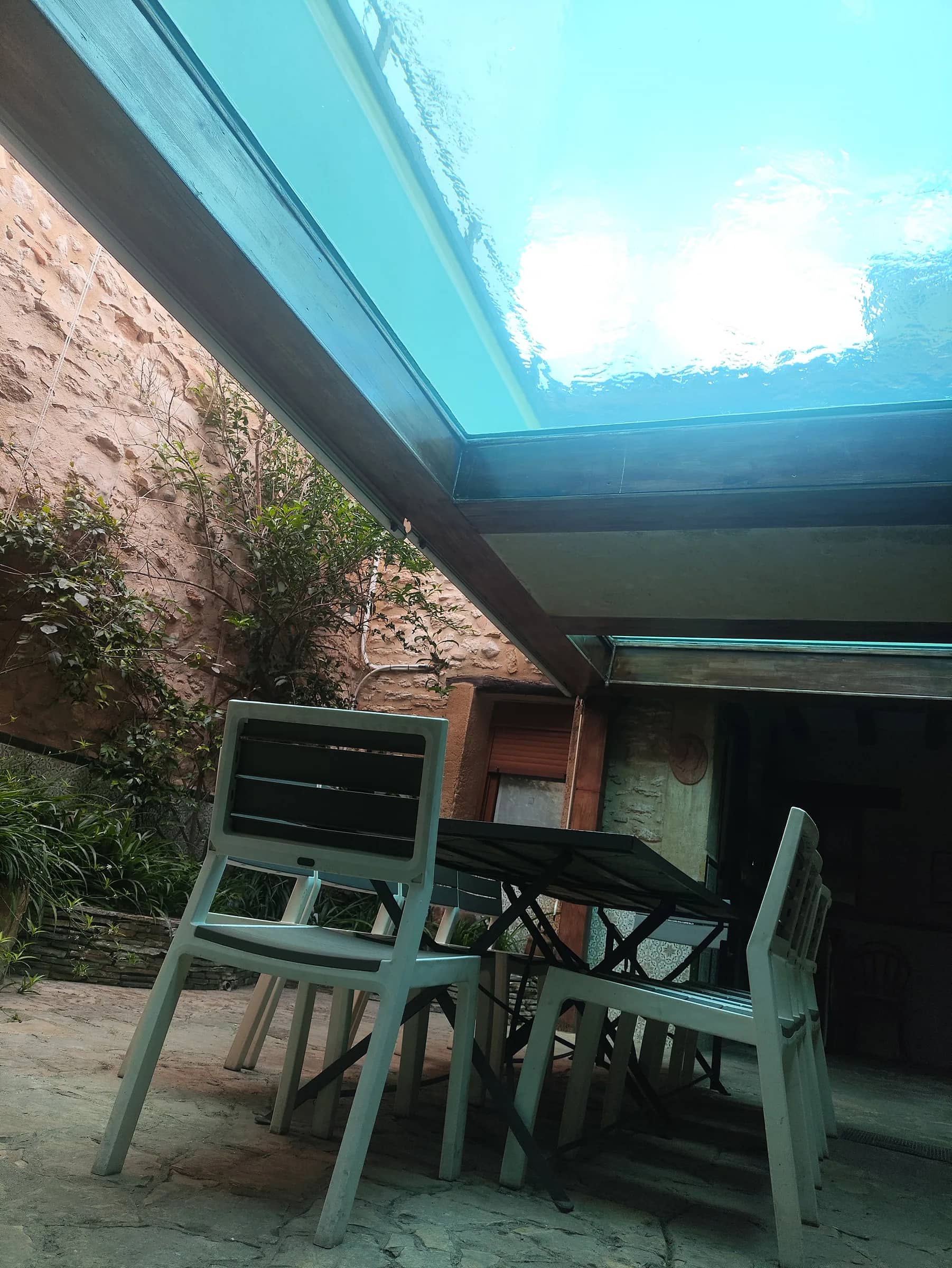Detalle del fondo de cristal de la piscina desde el patio, con mesa y sillas debajo