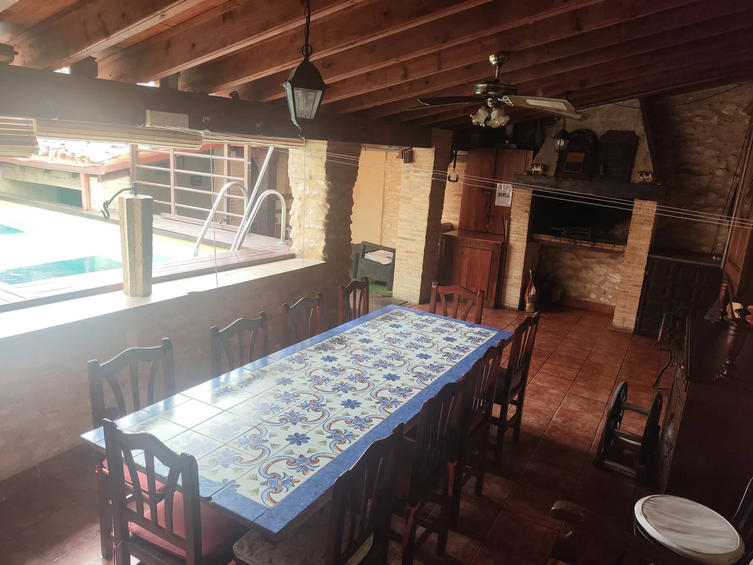Porche con barbacoa, mesa de azulejos para doce y ventanal a la piscina
